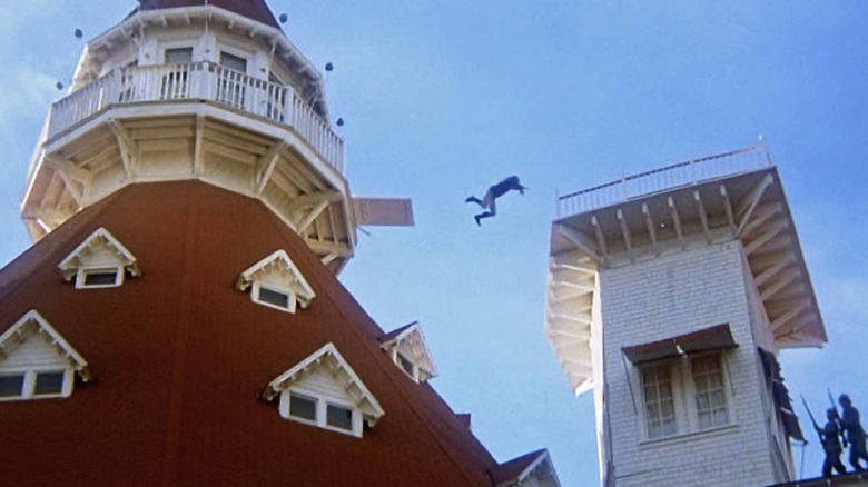 Steve Railsback as Cameron leaps from the roof of a house. to another roof in The Stunt Man