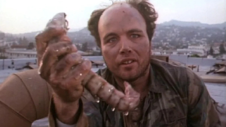 A homelass man holding up a big slimy worm creature in Silent Night, Deadly Night 4: Initiation