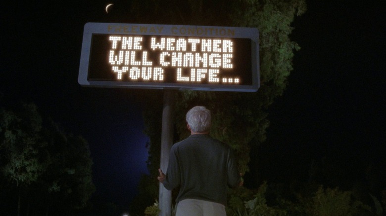 Harris Telemacher looking up at a freeway sign that says THE WEATHER WILL CHANGE YOUR LIFE in L.A. Story