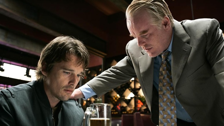 Ethan Hawke as Hank sitting at a table drinking a beer while Philip Seymour Hoffman as Andy touches his shoulder in Before the Devil Knows You're Dead