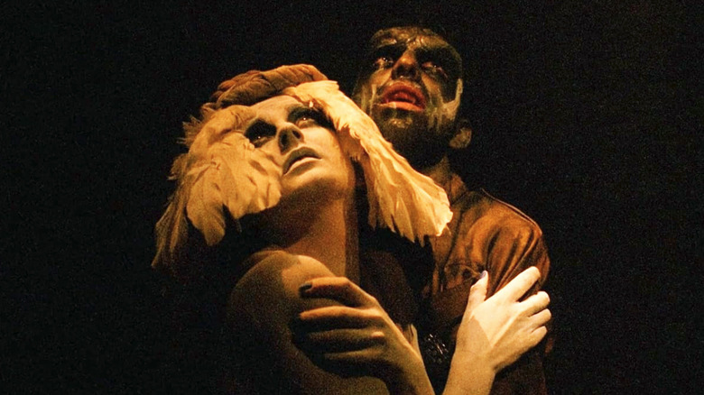 Two characters from Nightbreed embracing and illuminated by yellow light as they look skyward, surrounded by darkness