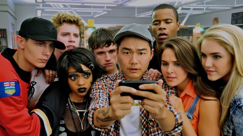 The teenagers in Detention are all gathered around a cell phone, looking at it intently