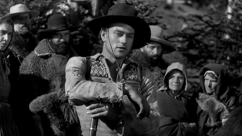 John Wayne's Breck Coleman leans on his rifle in front of a crowd in The Big Trail