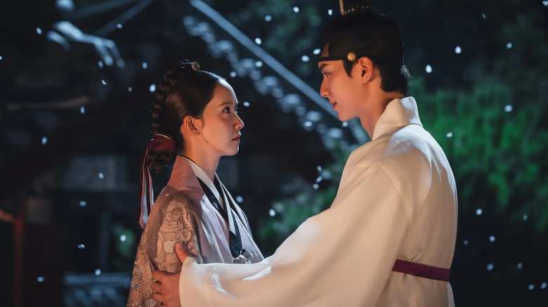 Yi Heon (Lee Chae-min) tenderly touches the arm of Yeon Ji-yeong (Im Yoon-ah) as petals fall around them in Bon Appétit, Your Majesty