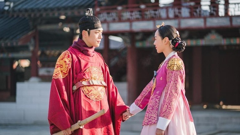 King Cheoljong (Kim Jung-hyun) holds the hand of Queen Cheorin (Shin Hye-sun) by an ornate palace in Mr. Queen