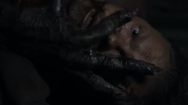 a man lying on a ship with a creature's hand on his face