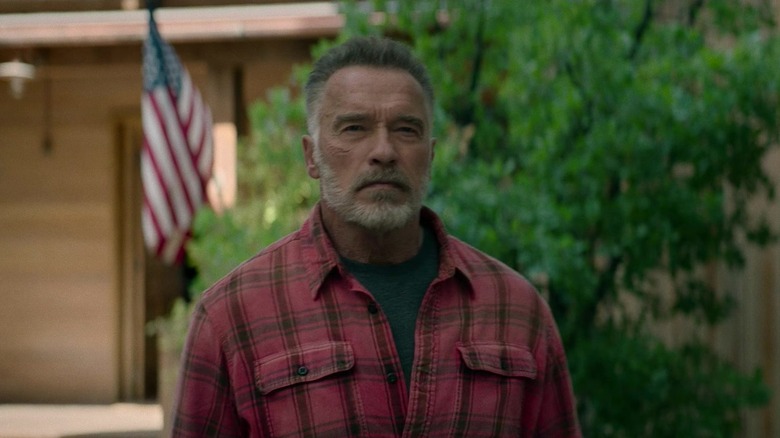 Arnold Schwarzenegger's Carl T800 stands in a suburban setting with a US flag visible in the background in Terminator Dark Fate.jpg