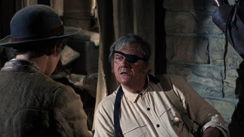 John Wayne's Reuben "Rooster" J. Cogburn looks shocked as he sits up while talking to Kim Darby's Mattie Ross in True Grit