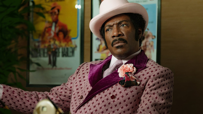 Eddie Murphy as Rudy Ray Moore sitting in his purple suit in Dolemite is My Name