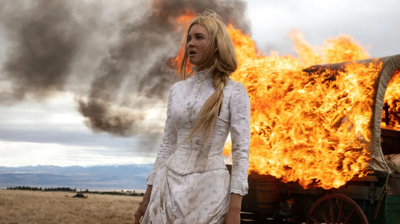 Isabel May as Elsa Dutton standing in front of a burning covered wagon on 1883
