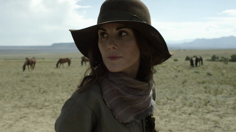 Michelle Dockery as Alice Fletcher standing in a field with horses and wearing a floppy hat in Godless