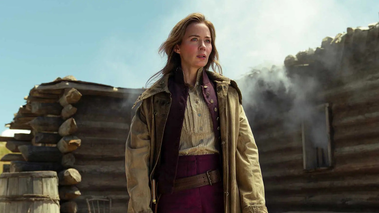 Emily Blunt as Cornelia Locke standing in front of a log building on The English