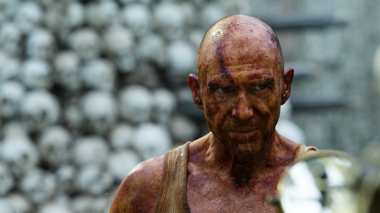 Ralph Fiennes as Dr. Kekson covered in iodine standing in front of the skull tower in 28 Years Later