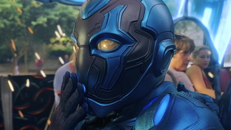 Xolo Maridueña as Blue Beetle putting his hand over his mouth on the bus in Blue Beetle