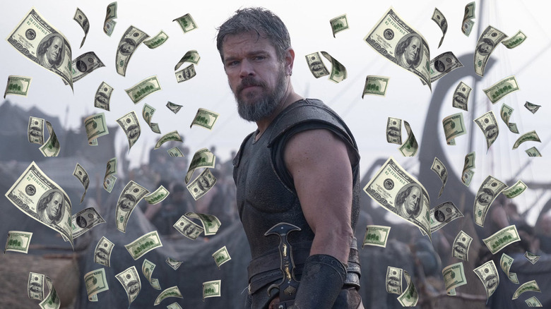 Matt Damon as Odysseus standing by his men on the beach surrounded by money in The Odyssey