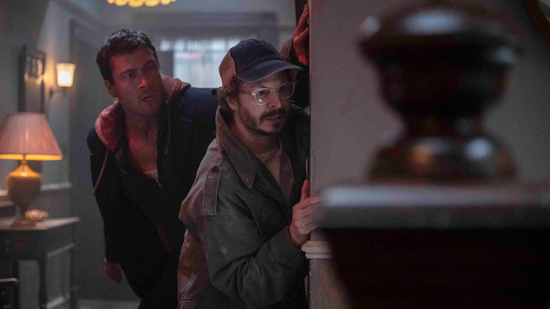 Glen Powell as Ben Richards hiding behind a wall with Michael Cera as Elton in The Running Man (2025)