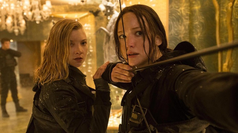 Jennifer Lawrence as Katniss getting ready to firee her bow as Natalie Dormer as Cressida holds her arm in The Hunger Games: Mockingjay - Part 2
