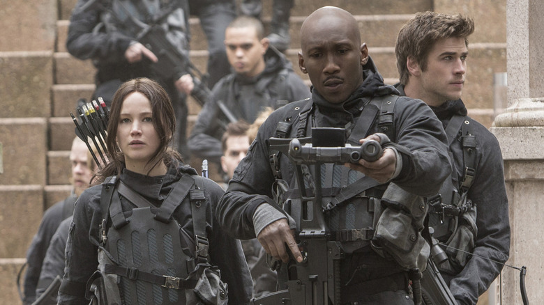 Jennifer Lawrence as Katniss walking by Mahershala Ali as Boggs, with Liam Hemsworth as Gale walking behind in The Hunger Games: Mockingjay - Part 2