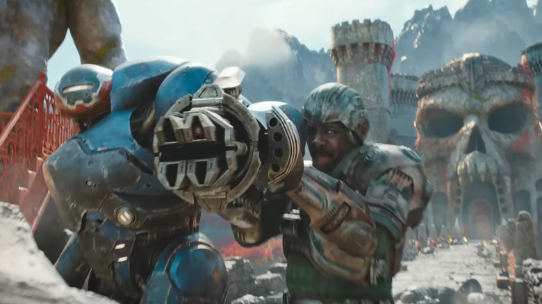 Roboto standing next to Idris Elba as Man-at-Arms as he's getting ready to fire a big gun in Masters of the Universe (2026)