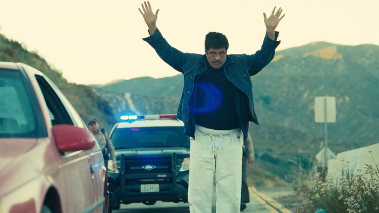 Benicio Del Toro as Sensei Sergio St. Carlos with his hands in the air about to be arrested in One Battle After Another
