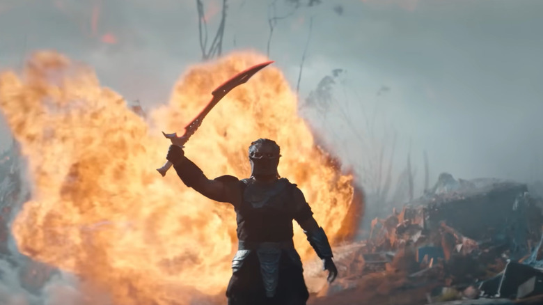 Dimitrius Schuster-Koloamatangi as Dek holding up his sword in front of an explosion in Predator: Badlands