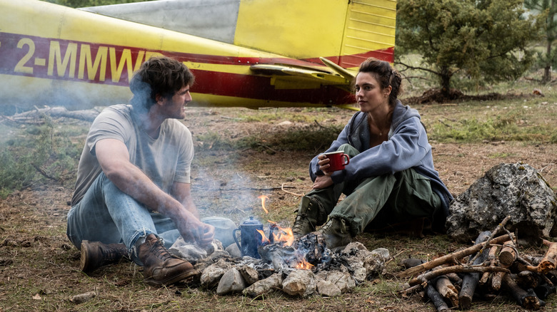 Jacob Elordi as Hig sitting next to Margaret Qualley as Cima by a fire in The Dog Stars