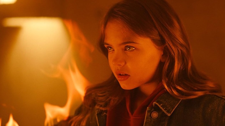 Ryan Kiera Armstrong as Charlie standing amidst the flames in Firestarter (2022)