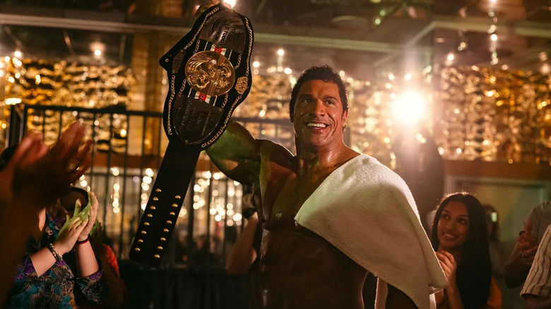 Dwayne Johnson as Mark Kerr holding up a champion belt in The Smashing Machine