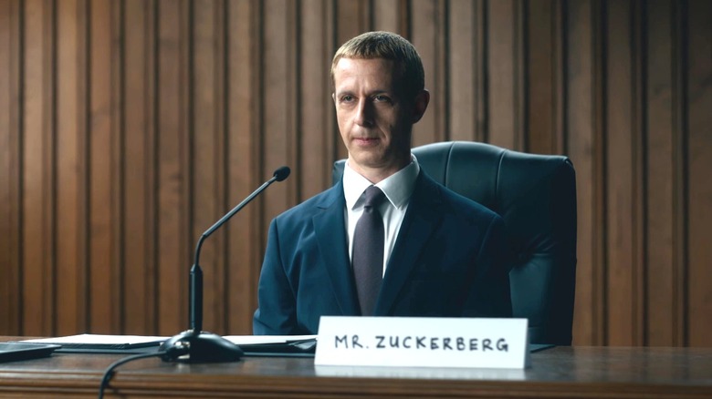 Jeremy Strong as Mark Zuckerberg sitting at a desk in front of a microphone in The Social Reckoning