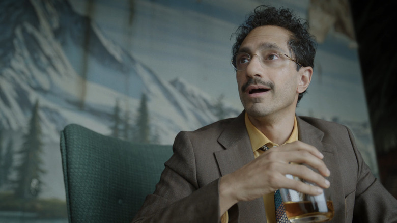 Riz Ahmed as Ganesh drinking whiskey while sitting at a table in Digger