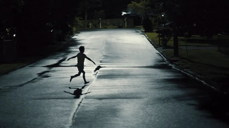A kid running across the street at night with his arms out in Weapons