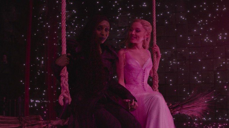 Cynthia Erivo as Elphaba sitting on a swing with Ariana Grande as Glinda in Wicked: For Good