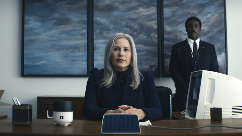 Patricia Arquette as Ms. Cobel seated behind a desk and Tramell Tillman as Mr. Milchick standing in the background in Severance