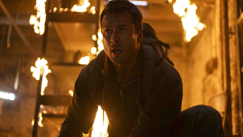 Glen Powell as Ben Richards crouching in front of a burning building in The Running Man