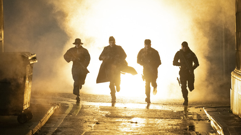 Four unnamed Hunters run down a rainy street holding weapons in The Running Man
