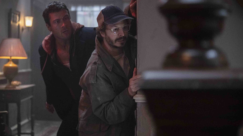 Glen Powell as Ben Richards and Michael Cera as Elton Parrakis creeping around a corner in a house in The Running Man