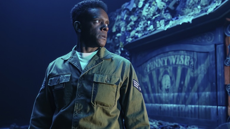 Chris Chalk as Dick Hallorann standing in front of a sign with a symbol of Pennywise in It: Welcome to Derry