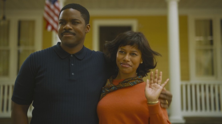 Jovan Adepo as Leroy Hanlon and Taylour Paige as Charlotte Hanlon standing in front of their home and waving in It: Welcome to Derry