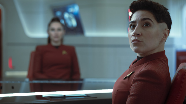 Melissa Navia as Ortegas sitting at a conference table with Christina Chong as La'an Noonien Singh in the background in Star Trek: Strange New Worlds