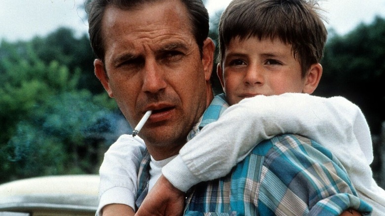 Butch Haynes (Kevin Costner) has a furrowed brow and a cigarette dangling from his mouth, carrying the child Phillip Perry (T.J. Lowther) on his back in A Perfect World