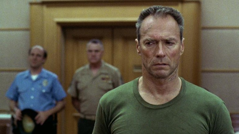Highway (Clint Eastwood) has a buzz cut and wears a green T-shirt, looking off to the left with a mix of confusion and intensity, two lawmen blurred in the background behind him in Heartbreak Ridge