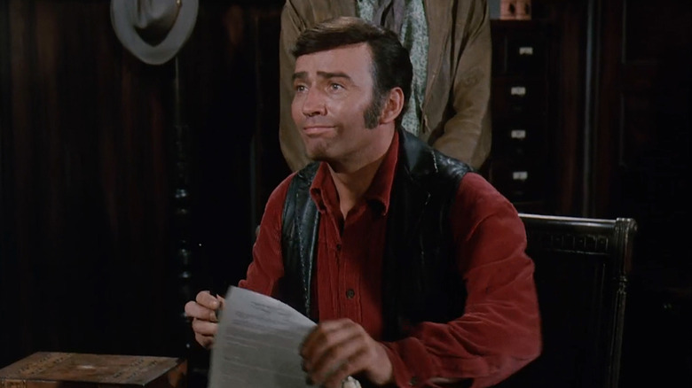 James Drury's Virginian looks up as he sits at a desk signing papers in The Virginian