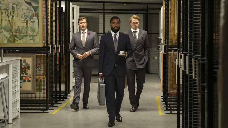 Jack Cutmore-Scott as Klaus, John David Washington as the Protagonist, and Robert Pattinson as Neil walking through a hallway filled with art in Tenet