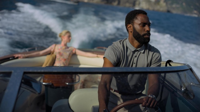 John David Washington as The Protagonist driving a boat with Elizabeth Debicki as Kat in the back in Tenet