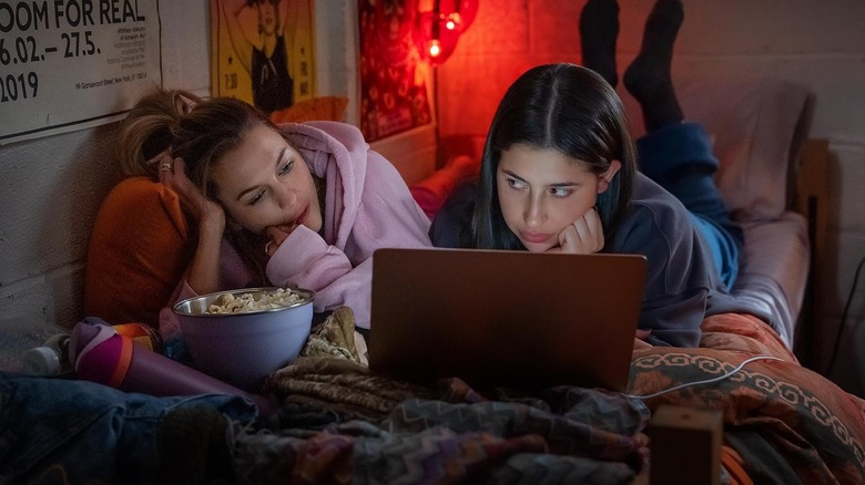 Chloe East as Celeste and Sadie Sandler as Devon lying on a bed watching a laptop together in Roommates