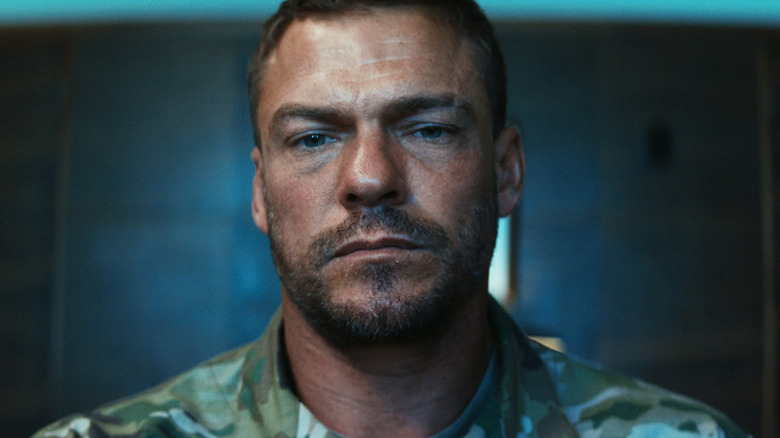 81 (Alan Ritchson) standing in a dark room in War Machine