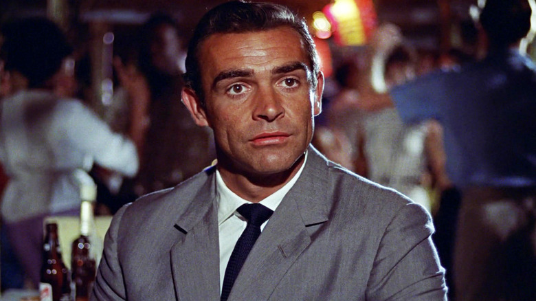 Sean Connery's James Bond sits in a suit looking across frame in Dr. No