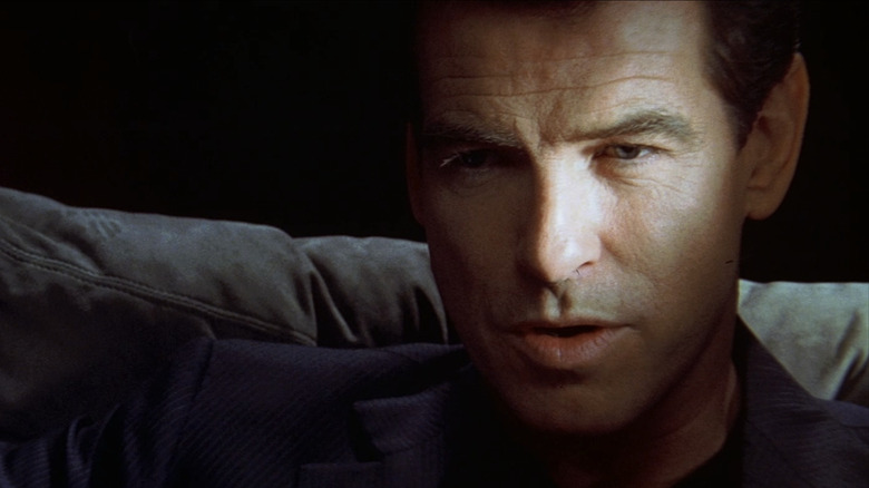 Pierce Brosnan's Thomas Crown has his face illuminated by bright light while he sits in a dark room in The Thomas Crown Affair