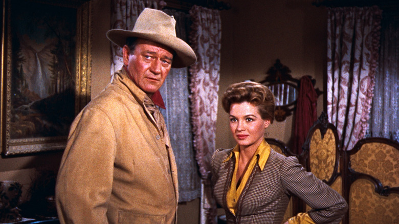 Sheriff John T. Chance (John Wayne) looks serious as he stands beside the cool and confident Feathers (Angie Dickinson) in an old Western-style dining room in Rio Bravo