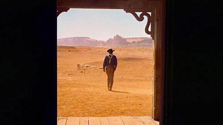 Framed by the doorway, Ethan Edwards, in a cowboy hat, walks alone toward the western desert in The Searchers